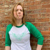 Redhead woman standing in front of brick wall wearing white and green raglan shirt with the green outline of an eagle on the front