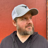 Bearded man standing in front of red wall wearing gray and white snapback hat with a black and white eagle on it